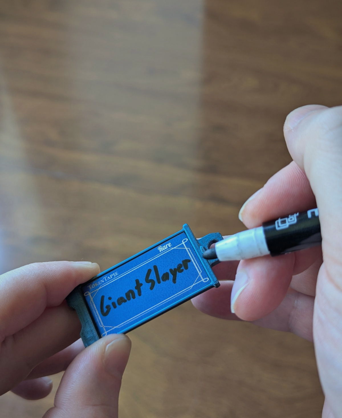 A hand writing Giant Slayer on a blue Rare TokenTab with a dry erase marker.
